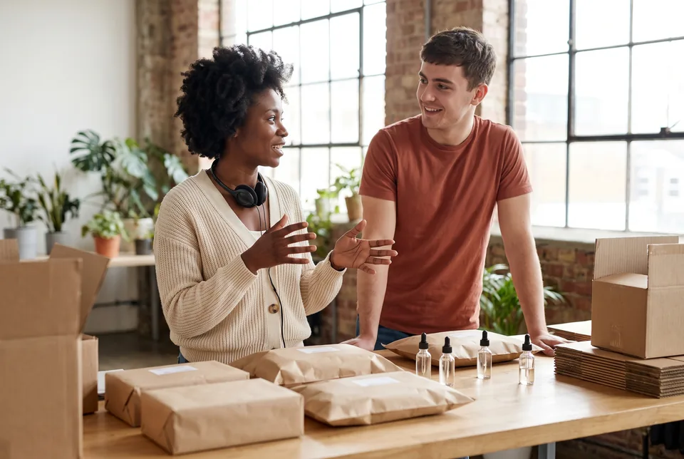 Support lead at a small online skincare brand talking through the support workload with a teammate in the packing studio