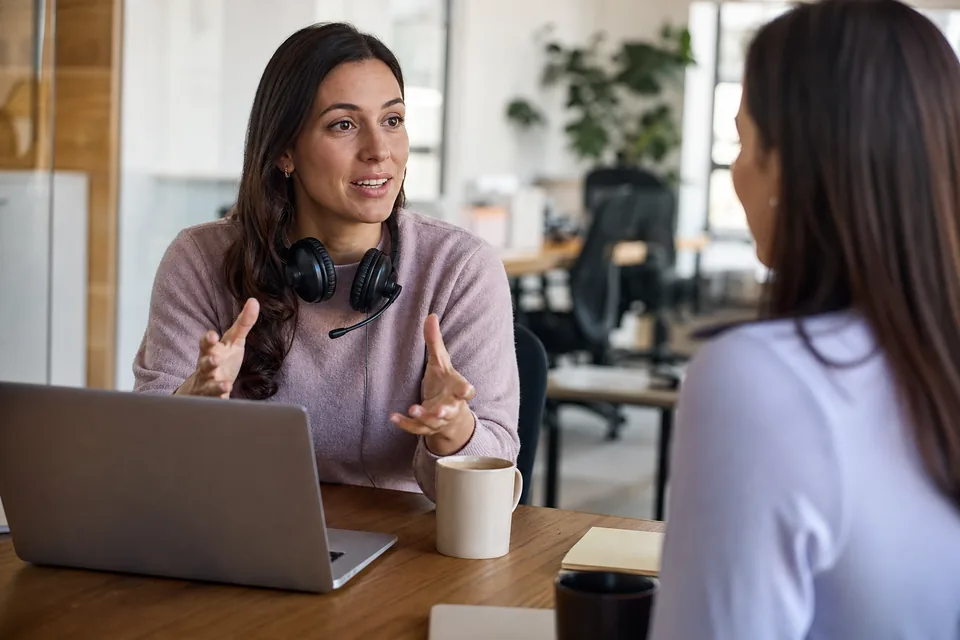 Support team lead with a headset discussing chat tooling with a colleague at an office table